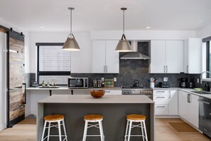 A modern kitchen with a central island, bar stools, pendant lighting, and a stone backsplash.