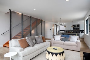 A modern living room with two sofas, a coffee table, and a staircase with a mesh partition.