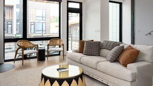 Ein modernes Wohnzimmer mit einer Couch, zwei Sesseln, einem Couchtisch und großen Fenstern mit Blick auf Gebäude.