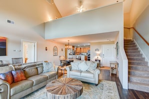 A spacious living room with a high ceiling, a dining area, and a kitchen in the background.