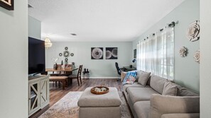 A living room with a sofa, a TV, a dining table, and decorative wall art.