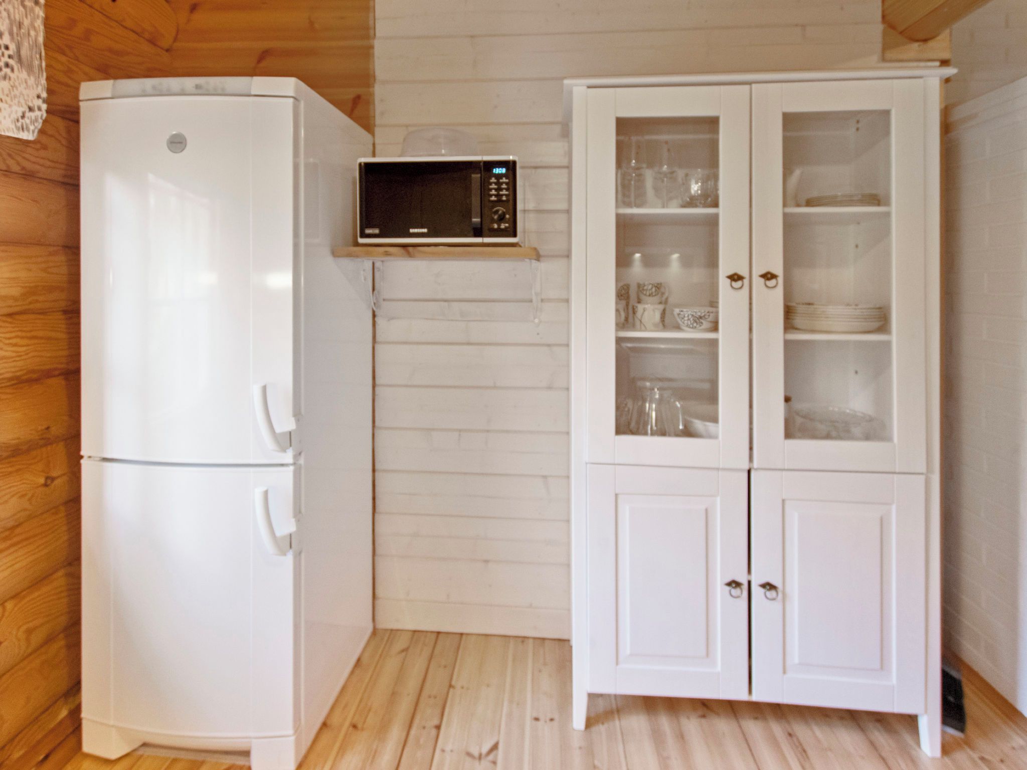 A compact kitchen with a white refrigerator, a microwave, and a cabinet with glass doors.