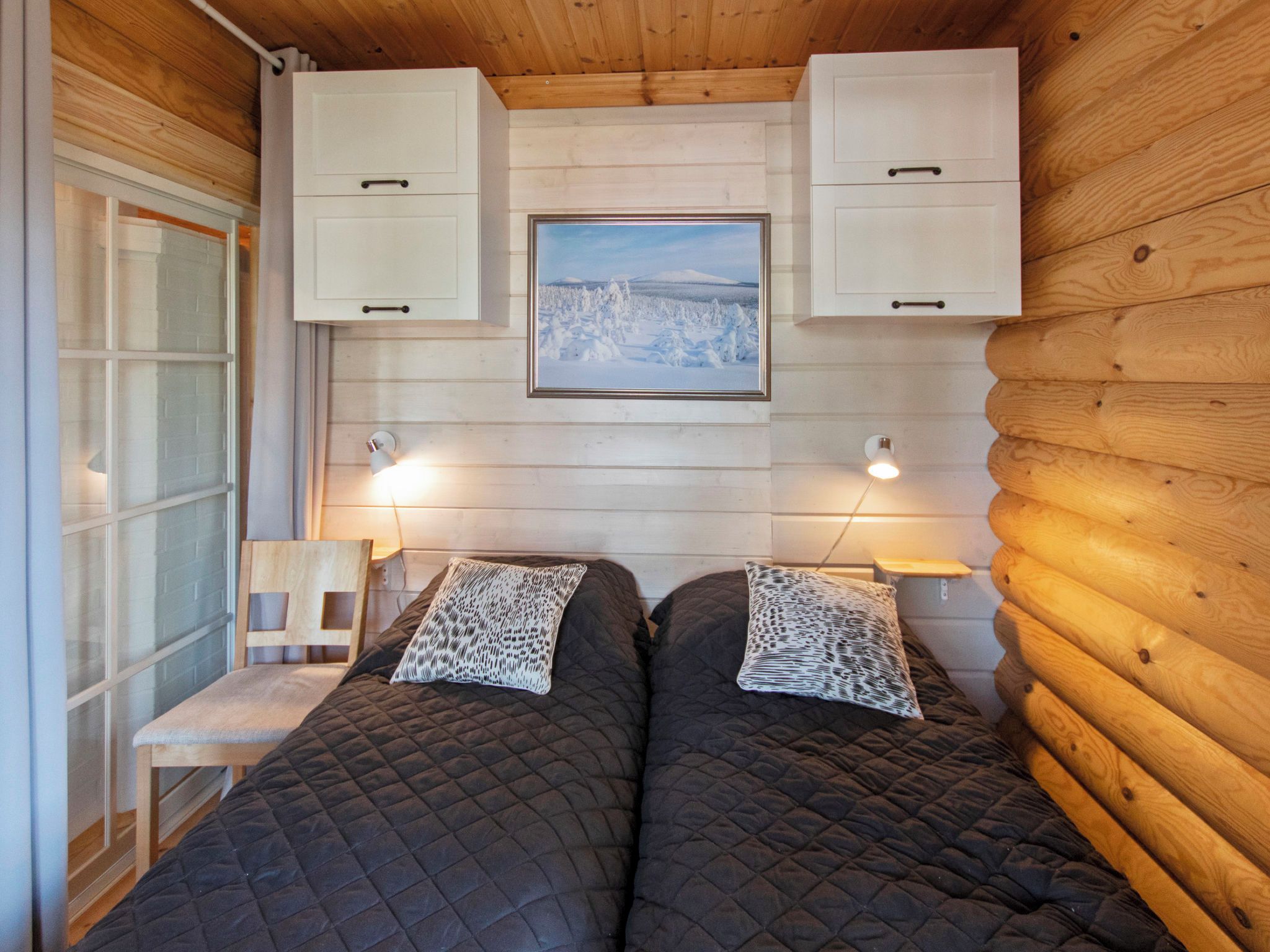 Une cabane avec deux lits, des murs en bois, une fenêtre et un tableau accroché au-dessus des lits.