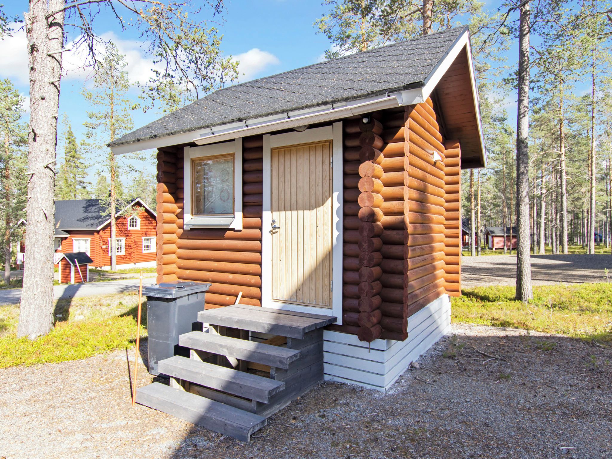 Hirsimökki, jossa on puuovi, ikkuna ja pieni kuisti, jonka portaat johtavat ovelle.
