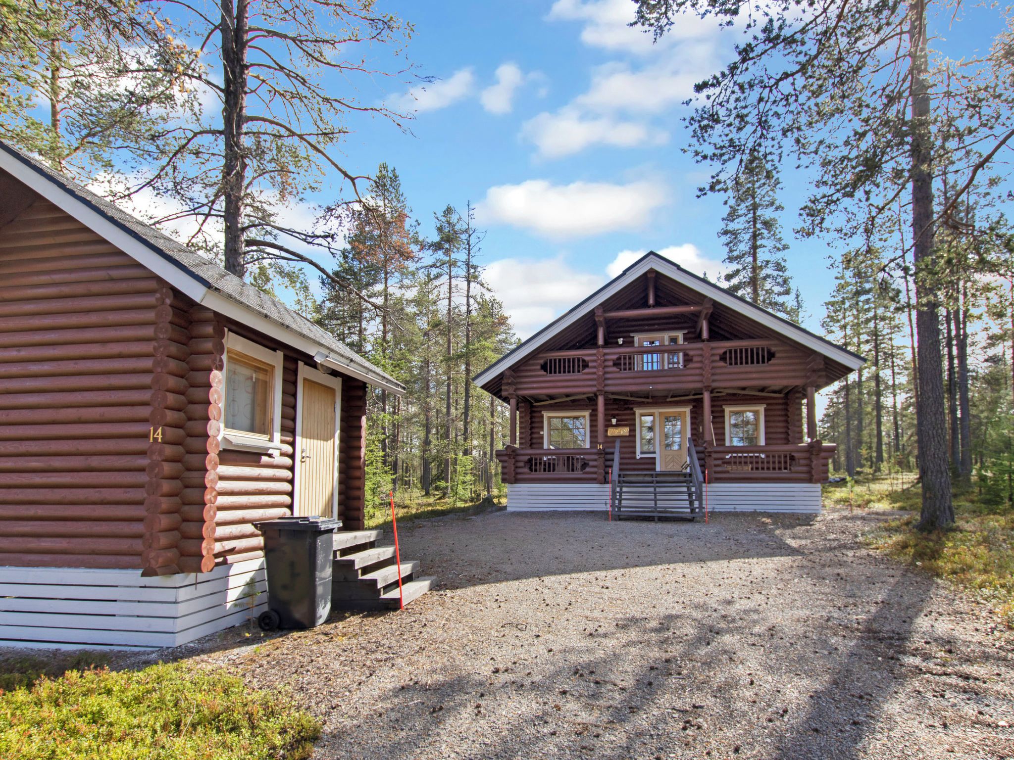 A two-story log cabin with a porch and a gravel driveway.