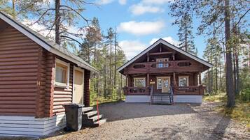 A two-story log cabin with a porch and a gravel driveway.