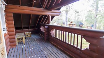 Um deck de madeira com mesa, bancos, guarda-corpo e vista para uma área arborizada com cabanas.