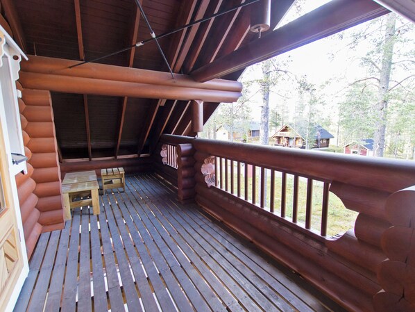 A wooden deck with a table and benches, a railing, and a view of a forested area with cabins.