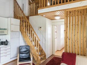 A staircase leading to a second floor, a kitchen area with a microwave, a refrigerator, and a chair.