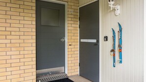 A door with a metal handle and a small step leading up to it, a black doormat, and a pair of skis leaning against a white wall. - Kivakatti by Interhome (Sotkamo)