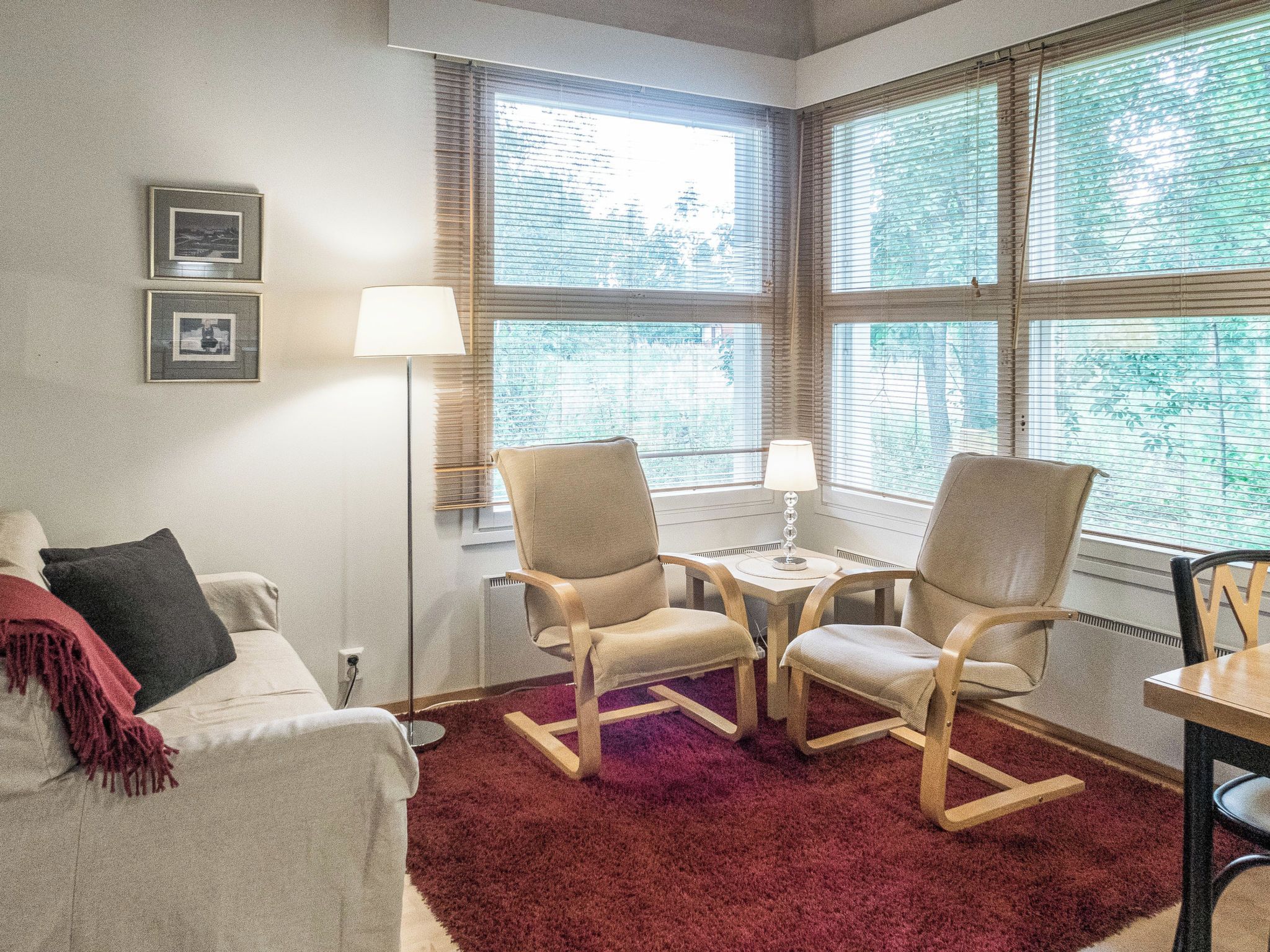 Una habitación con un sofá blanco, dos sillones, una mesita y una alfombra roja.
