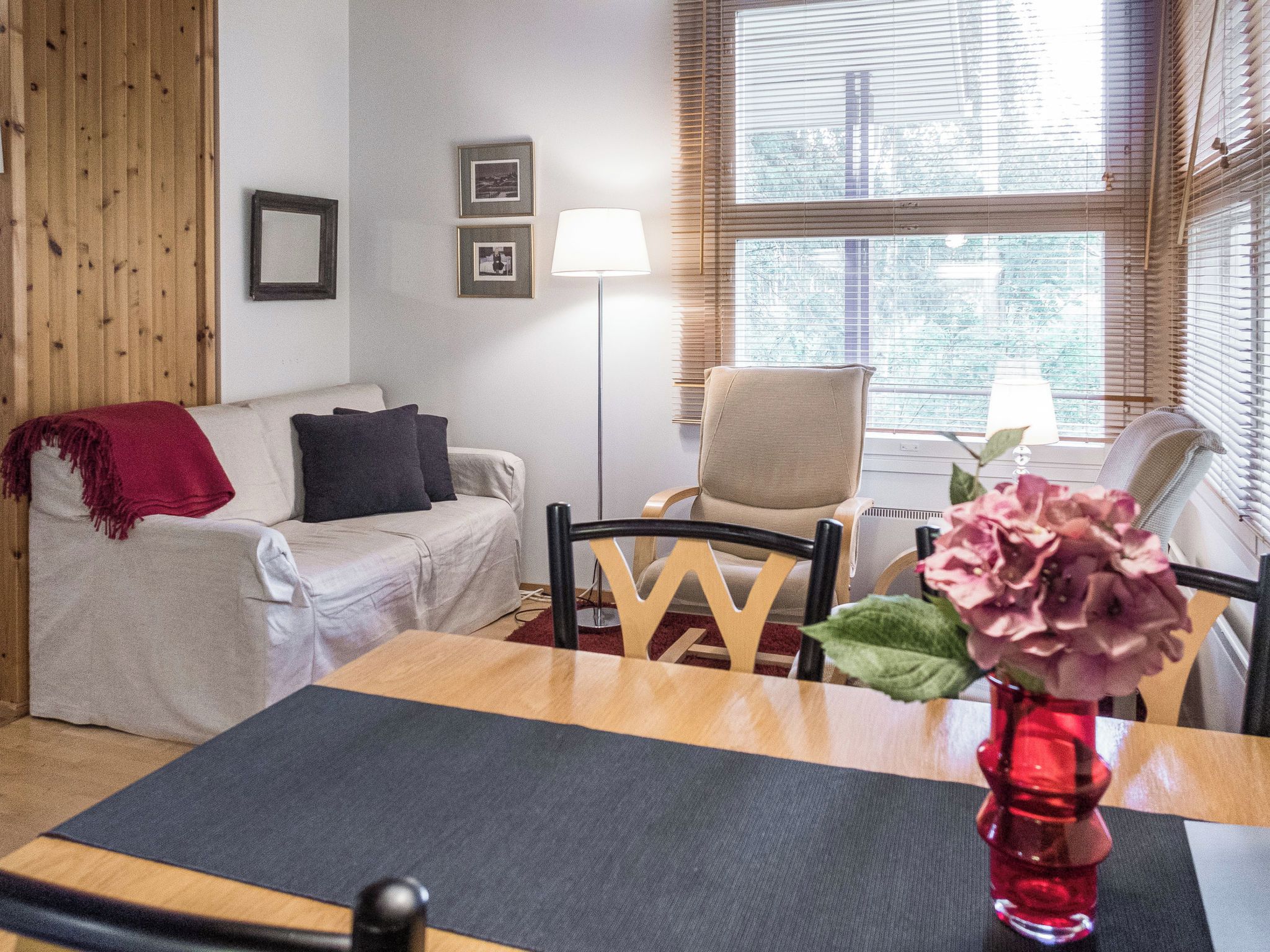 A furnished room with a sofa, a chair, a dining table, and a window with blinds.