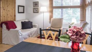 A furnished room with a sofa, a chair, a dining table, and a window with blinds.