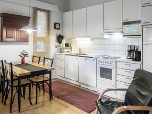 A modern kitchen with white cabinets, a stove, and a microwave. There is a dining table with chairs and a red rug on the floor.