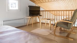A cozy attic bedroom with a sloped ceiling, a bed, a TV on a wooden stand, a rocking chair, and a small table. - Kivakatti by Interhome (Sotkamo)