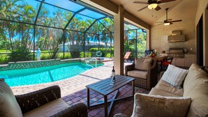 An outdoor patio with a pool, wicker furniture, ceiling fans, and a view of a tropical garden.