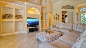 A living room with a large flat-screen TV, a beige sofa, and a fireplace.