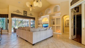 A spacious living room with a large sofa, a ceiling fan, and a view of the outdoors through large windows.