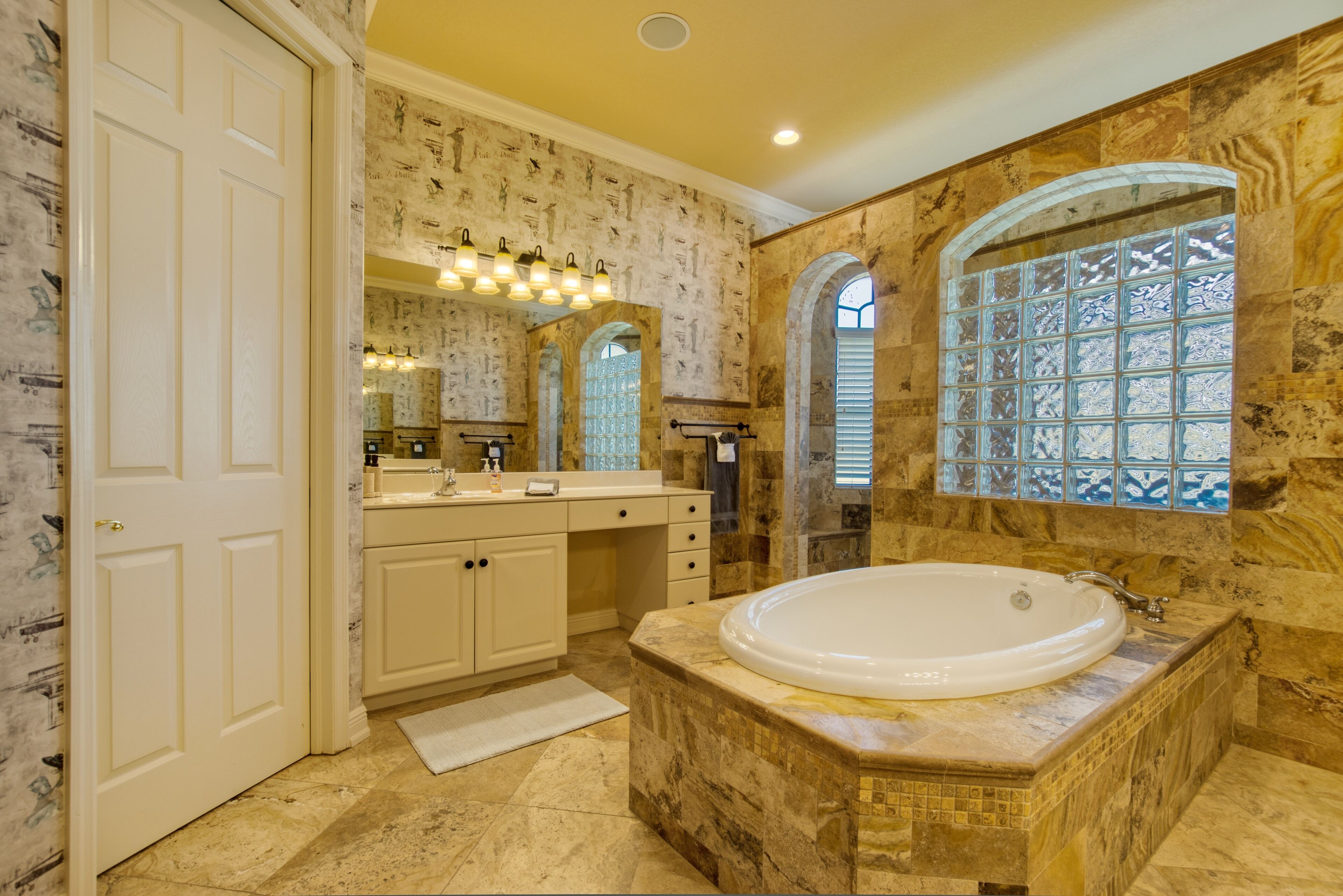 Une salle de bain dotée d’une grande baignoire, d’un meuble-lavabo avec un miroir et d’une fenêtre ornée de motifs décoratifs en verre.