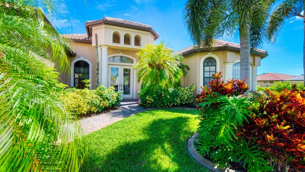 A house with a well-maintained lawn, palm trees, and a variety of colorful plants.