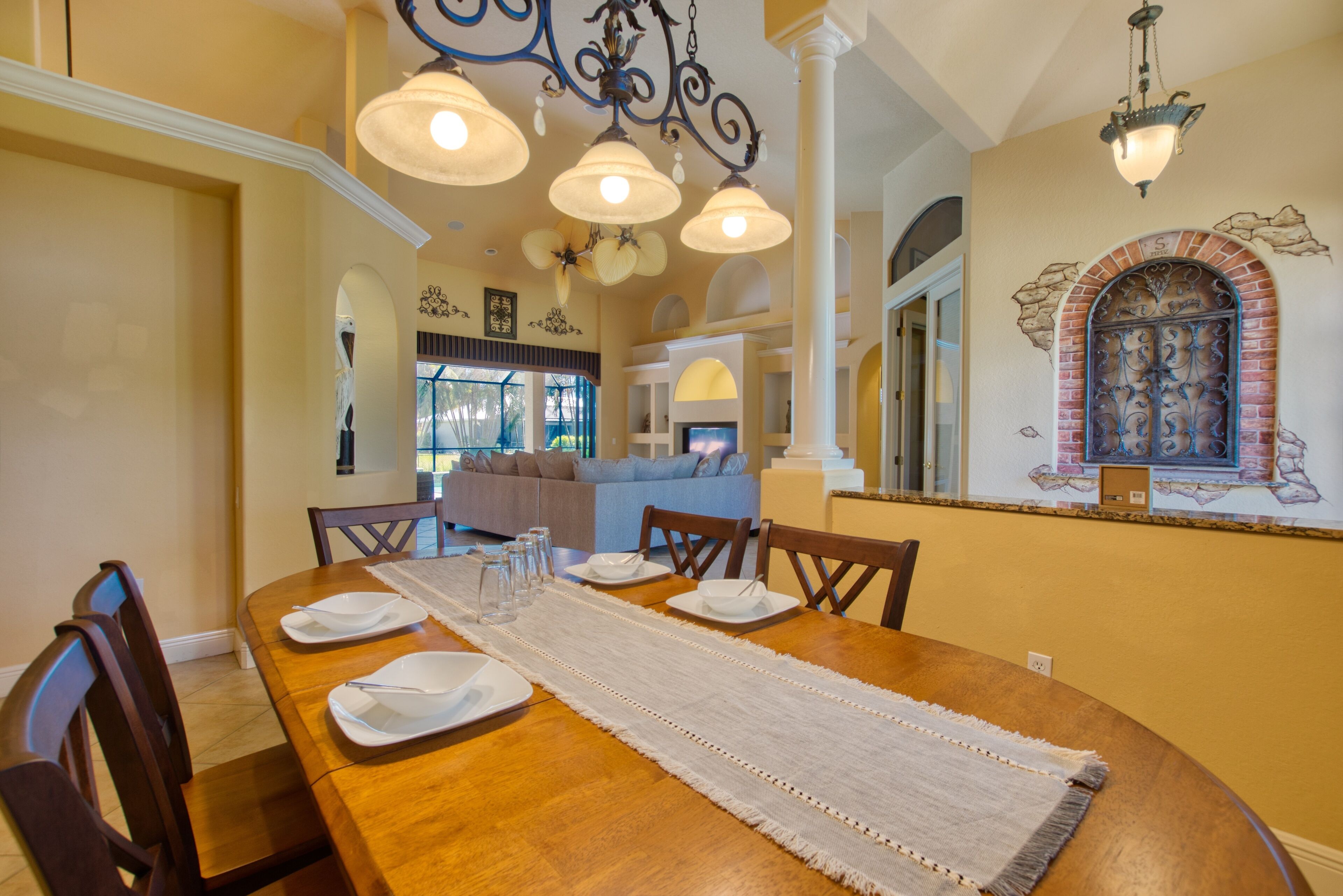 A dining area with a wooden table set for four, surrounded by chairs, with a white runner and glassware.