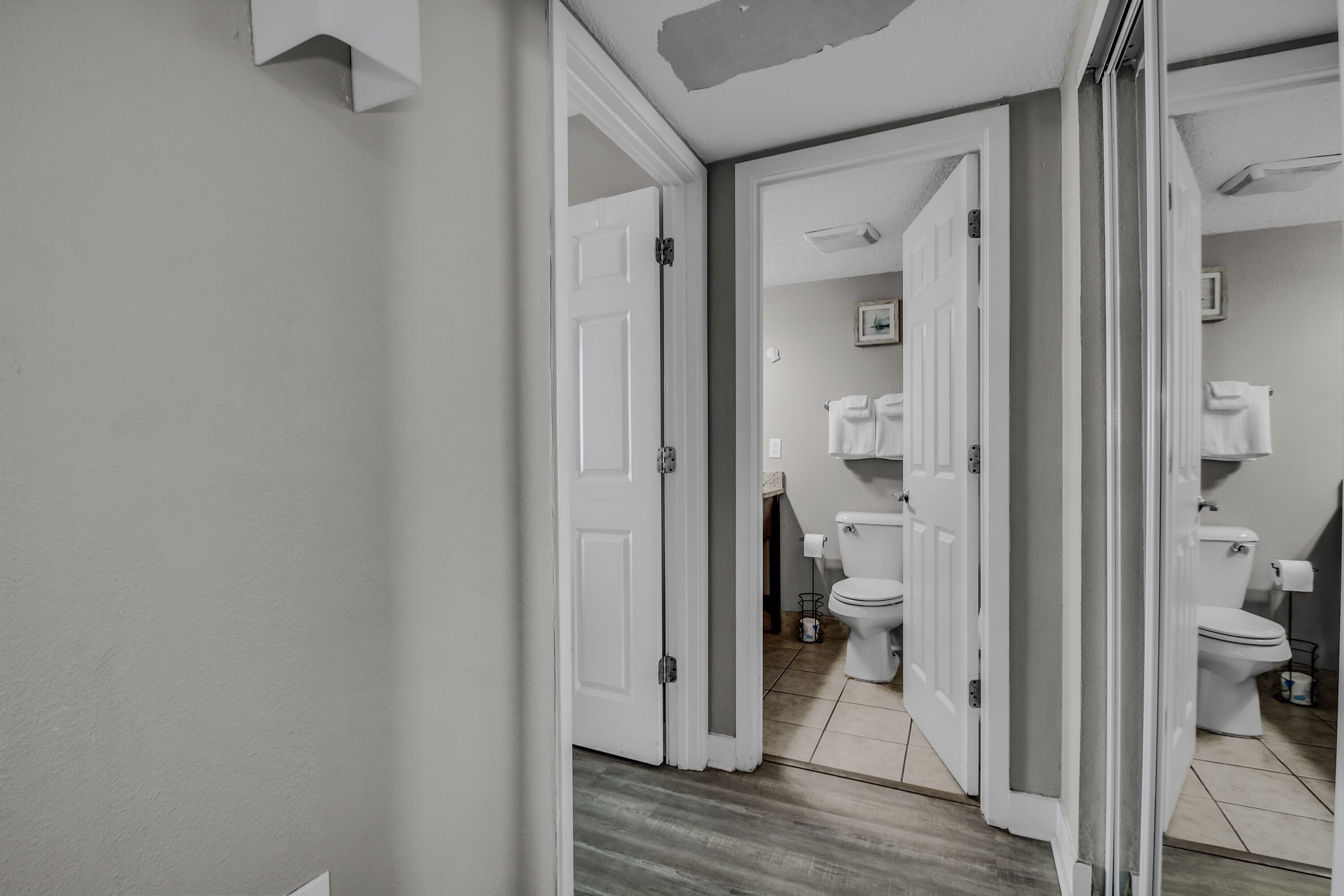 A hallway leading to a bathroom with two toilets, a sink, and a mirror.