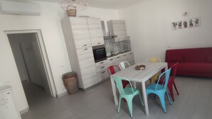 A compact kitchen with white cabinets, a red sofa, and a dining area with colorful chairs. - Donna Beatrice AmMare beach house (Donnalucata)