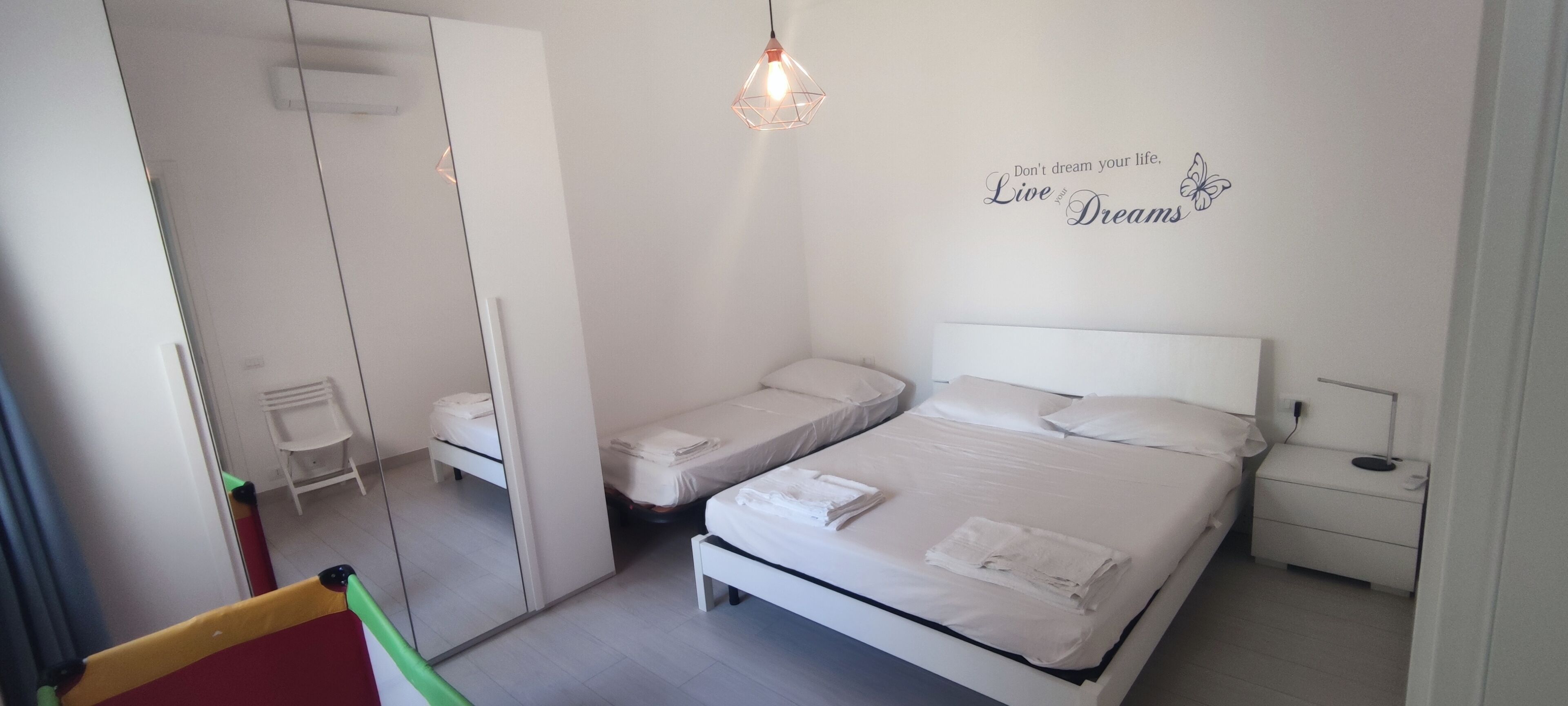 A bedroom with a bed, a nightstand, a mirror, and a wall decoration.