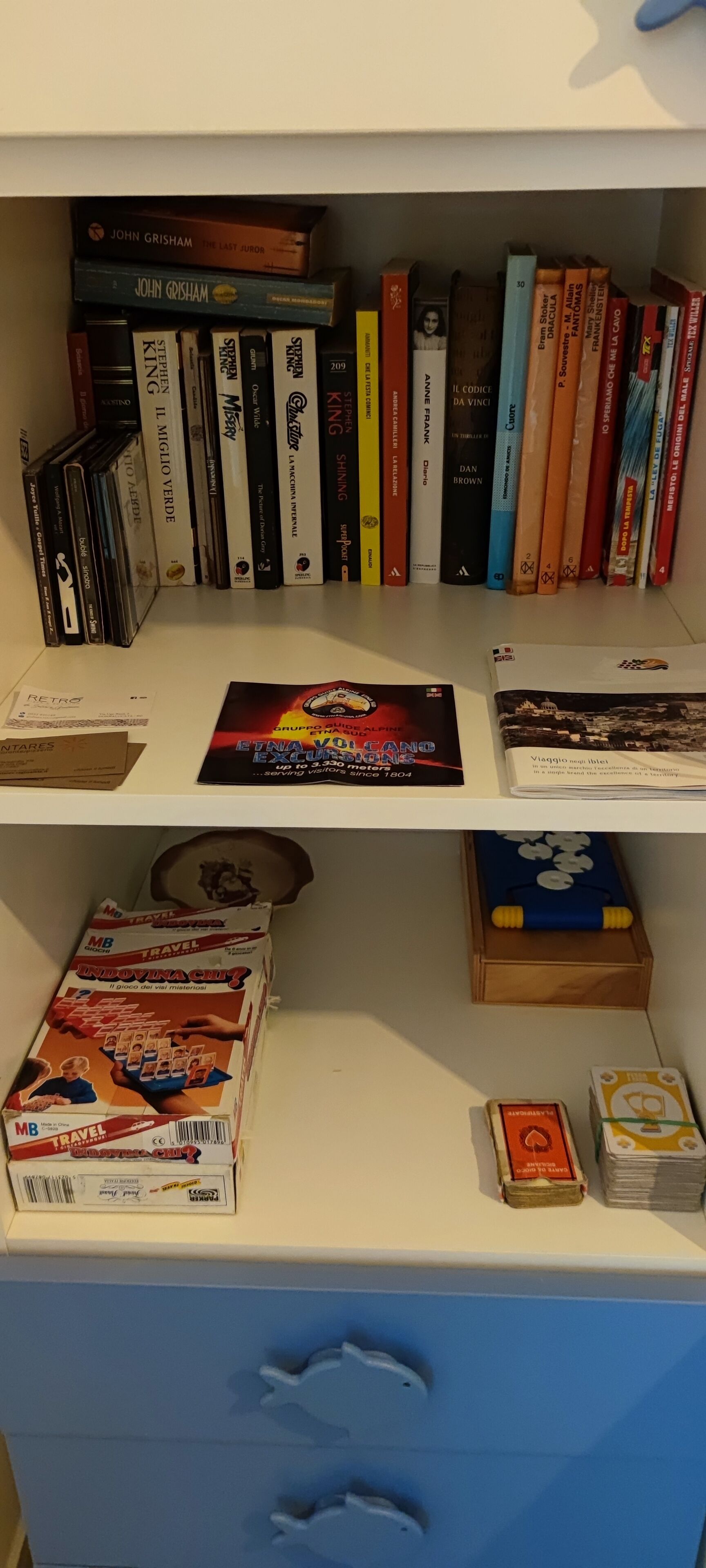 Una libreria con diversi libri e riviste, un gioco da tavolo e un piccolo mazzetto di carte da gioco.