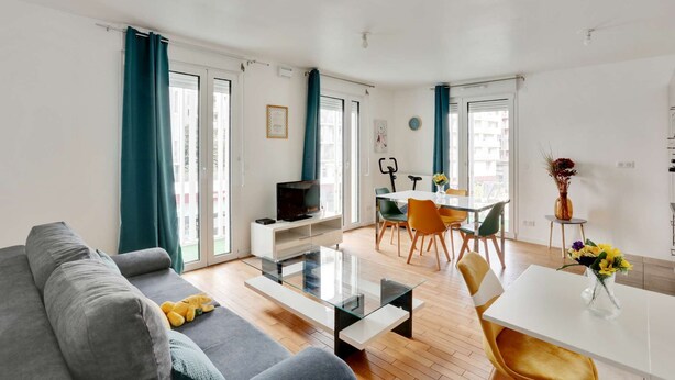 A modern living room with a sofa, coffee table, TV, and dining area with chairs and a table. - Chic apart with parking near Paris (Nanterre)
