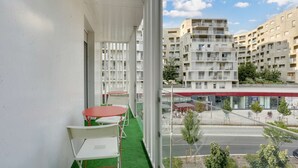 A balcony with a red table and white chairs, overlooking a street with buildings and a bar. - Chic apart with parking near Paris (Nanterre)