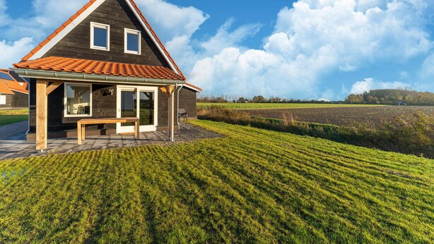 Une maison avec un toit en pente, une véranda et une vue sur un champ cultivé.