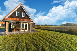 A house with a sloped roof, a porch, and a view of a cultivated field. - Spacious holiday home with sauna (Scherpenisse)