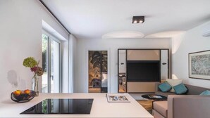 A modern living room with a large TV, a sofa, a coffee table, and a kitchen area with a white countertop. - Belvilla by OYO Palm Loggia (Meran)
