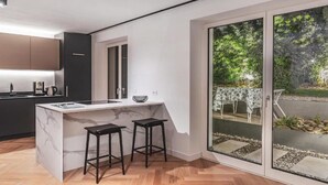 A modern kitchen with a marble island, black stools, and a view of a garden through a glass door. - Belvilla by OYO Palm Loggia (Meran)