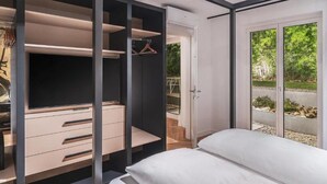 A modern bedroom with a large bed, a walk-in closet with multiple drawers and shelves, and a sliding glass door leading to a garden. - Belvilla by OYO Palm Loggia (Meran)