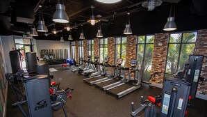 Una palestra con tapis roulant, macchinari per pesi e un muro di mattoni con finestre.