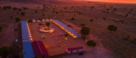 An aerial view of a campsite with tents arranged in rows, a central gathering area, and a few trees scattered around.
