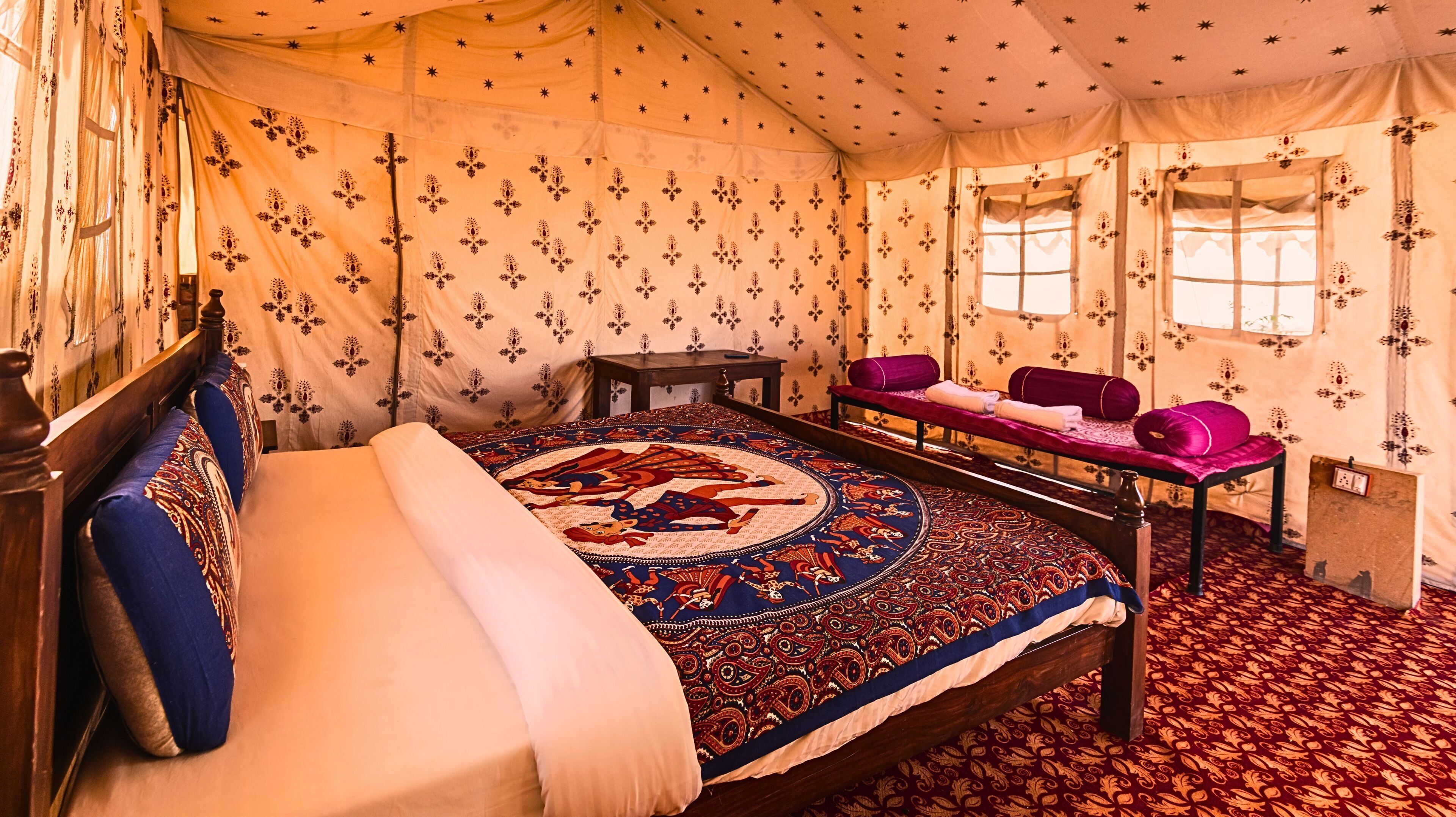 Una habitación tradicional con cama, una mesa con cojines y cortinas estampadas.