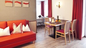 Una sala de estar moderna con un sofá rojo, una mesa de comedor con sillas y un frutero.