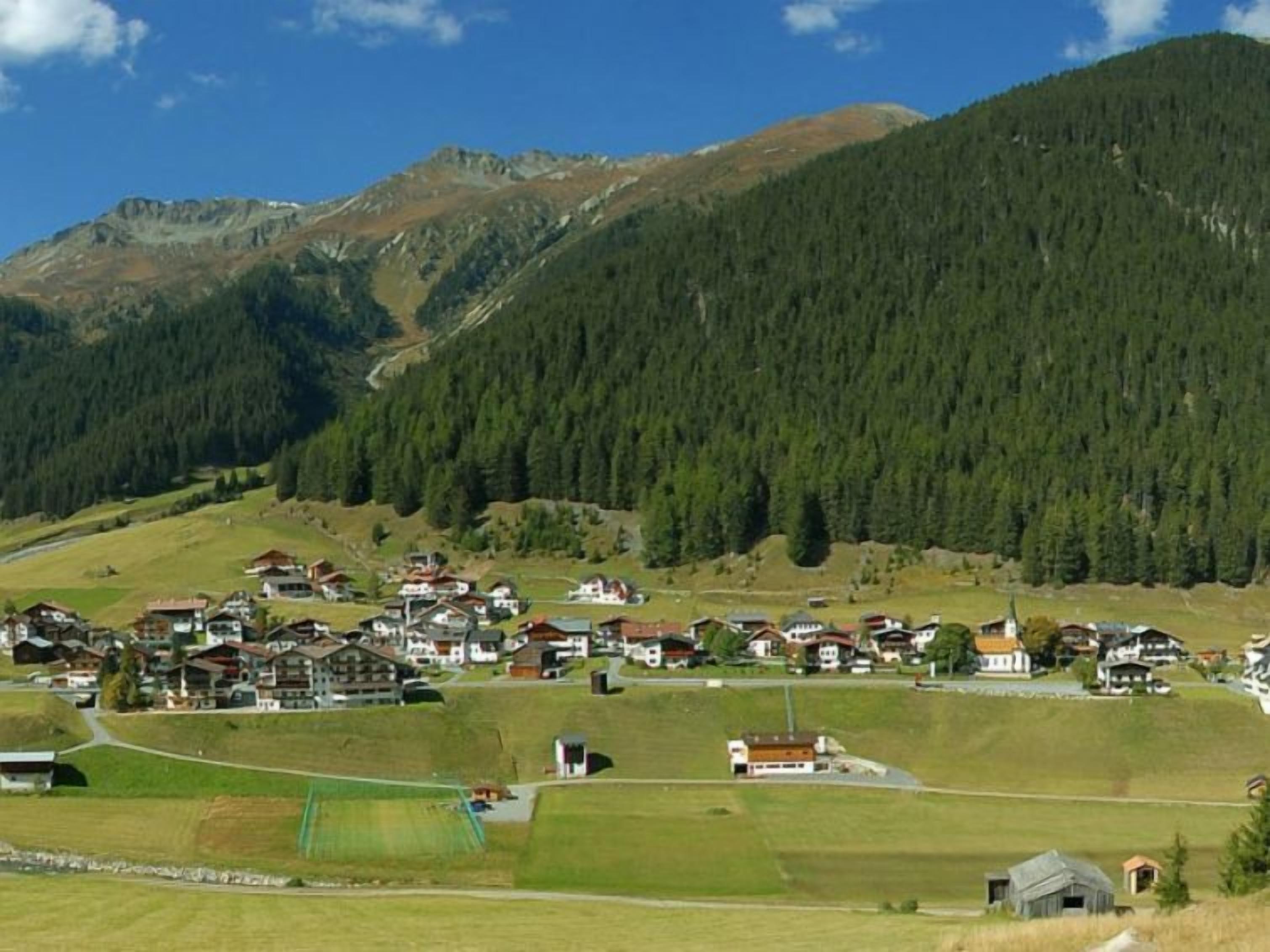 A mountainous village with houses spread across the valley, surrounded by dense forests and hills.