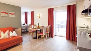 Una sala moderna con un sofá rojo, una zona de comedor con mesa y sillas, y una cocina con fregadero y armarios.