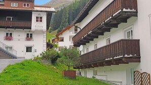 Un hotel con fachada blanca, balcones de madera y montañas al fondo.