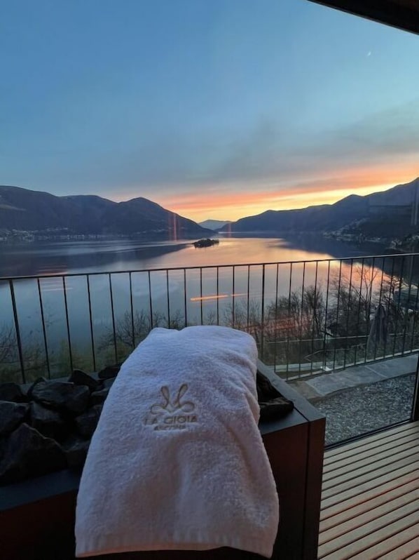 Un balcon avec une serviette, donnant sur un lac paisible et des montagnes au coucher du soleil.