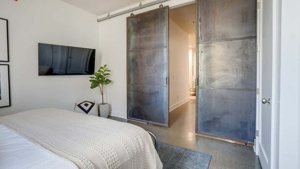 A bedroom with a bed, a sliding door, a television, and a plant. - Lofts at 30th-Urban Nest-4 Mins to Broadway! (Nashville)
