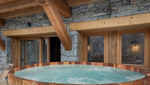 Een hottub met een houten buitenkant, gelegen tegen een stenen muur en houten balken.