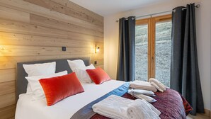 Een hotelkamer met een houten hoofdbord, een bed met witte en rode kussens, een rode en blauwe dekbedovertrek en een raam met donkere gordijnen.