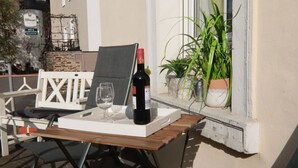 A table set with a bottle of wine and two glasses, positioned near a window with potted plants. - Beautiful apartment with a view of the vineyards/on the banks of the Moselle/2 terraces just for you (Bruttig-Fankel)