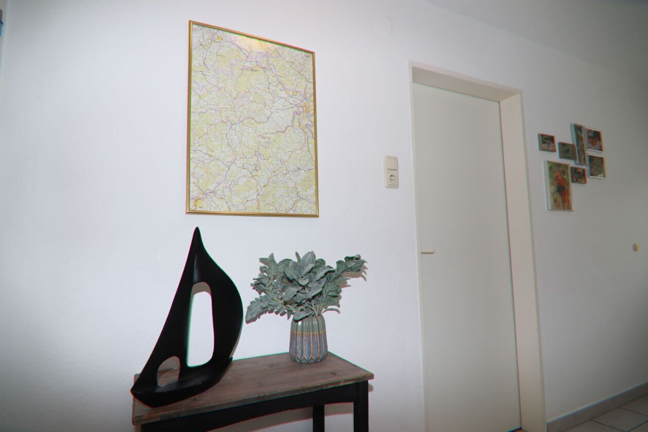A hallway with a map on the wall, a sculpture on a table, and a door with pictures on the wall.