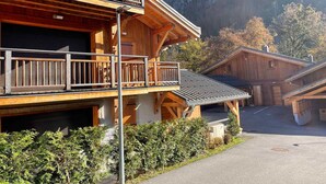 A wooden chalet with a balcony, surrounded by lush greenery and a mountainous backdrop. - Luxurious Mountain Apartment, 2 Beds, Terrace + High-End Amenities, Close to Village & Ski Bus (Samoëns)